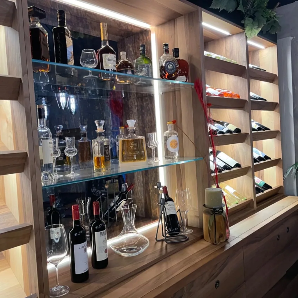 Beleuchtete Bar und Weinregal im Restaurant mit Weinflaschen, Grappa und Glaskaraffe.