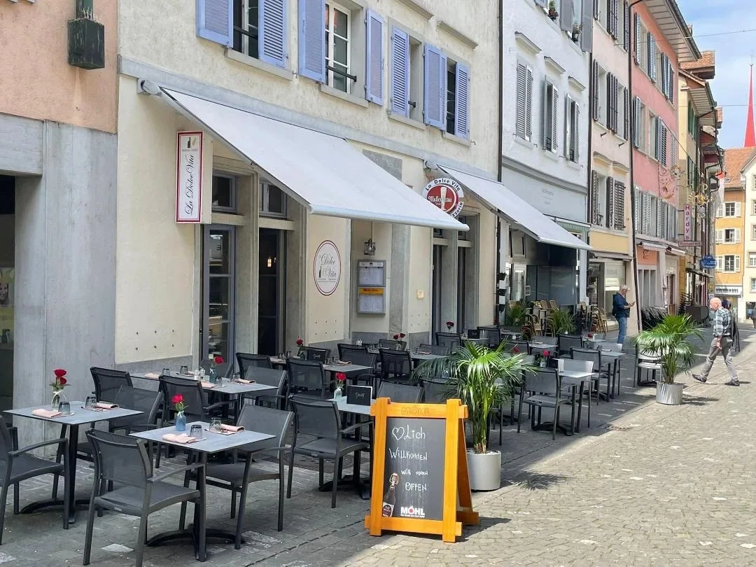 Sonnige Restaurant-Terrasse in der autofreien Marktgasse in Bremgarten mit Markisen, Tischen und Willkommenstafel.